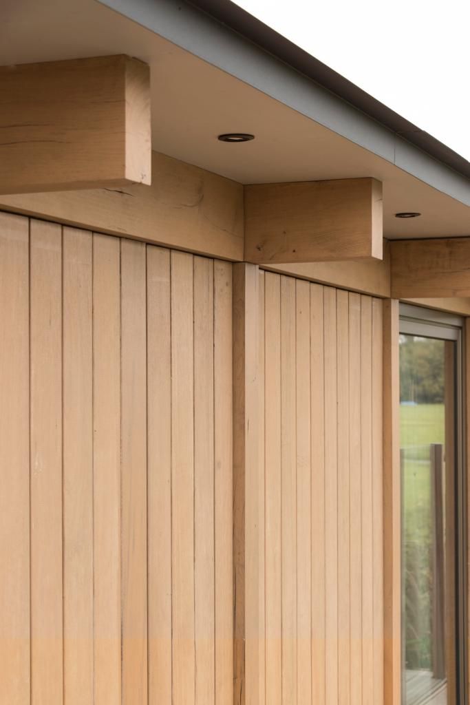 Eiken balkkoppen onder de dakrand van een drijvende woning, boven een gevel van eiken delen