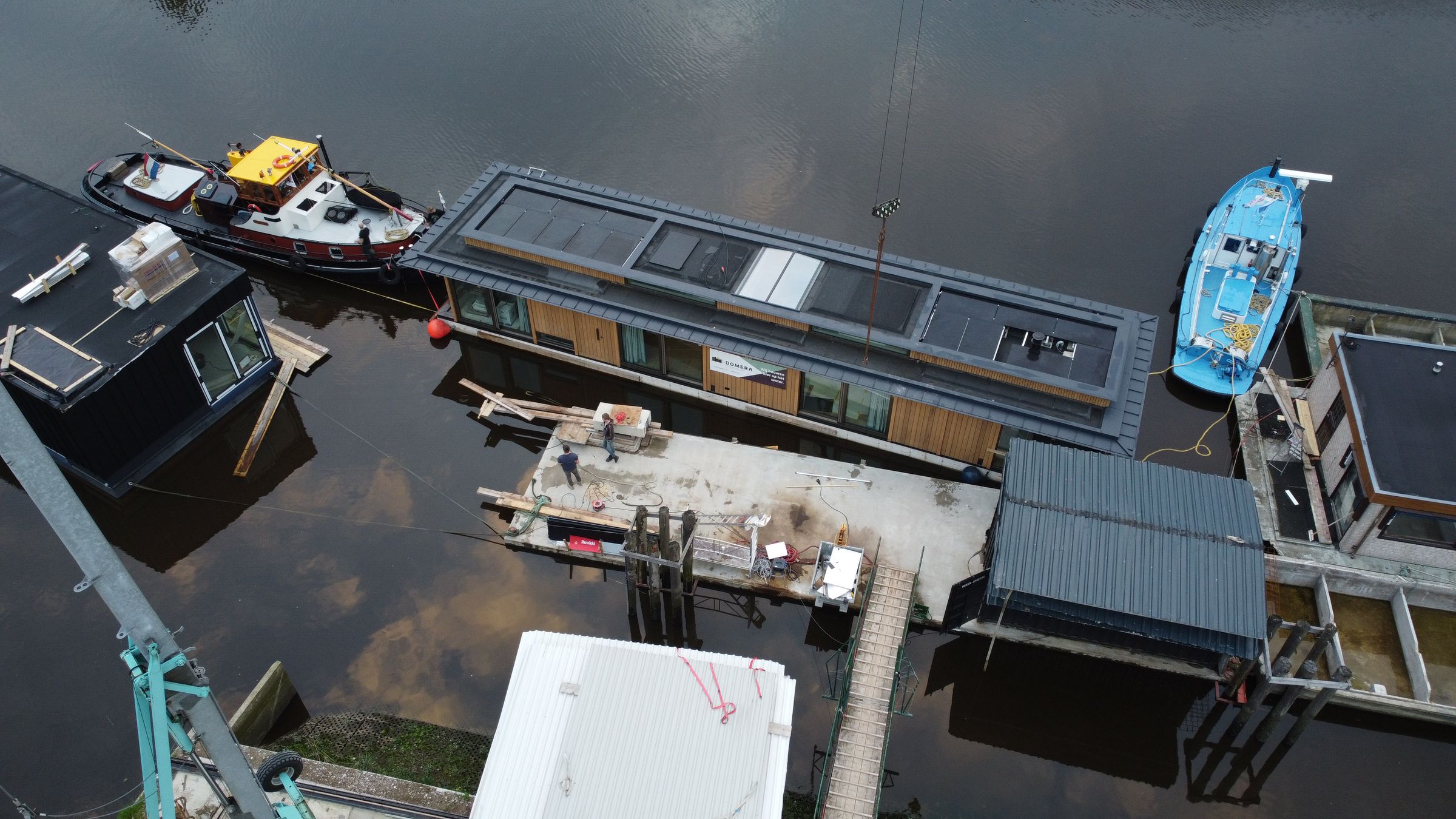 Luchtfoto van de werf in Gouda met drijvende woningen in aanbouw, een steiger en een sleepboot