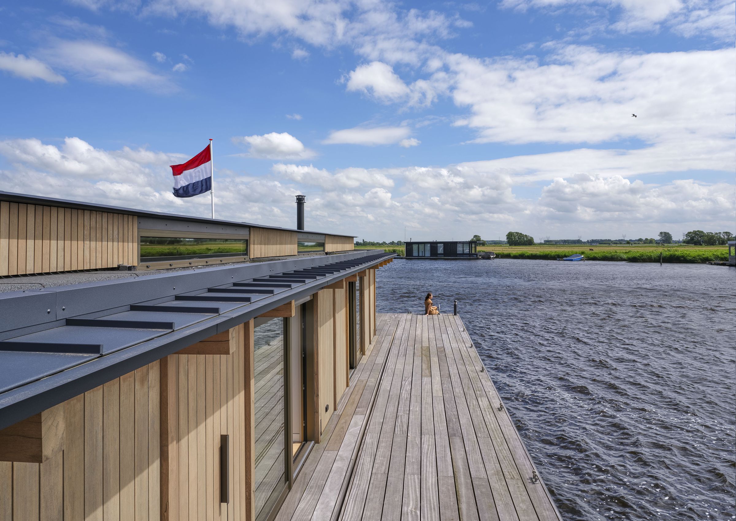 Het lange houten terras aan de waterkant, met de vlag en de polder aan de overkant